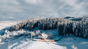 A snow-covered landscape with a modern building surrounded by a forest. - Tuğra Butik Otel (Savsat)
