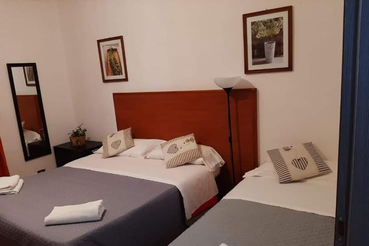 A hotel room with two beds, a nightstand with a lamp, and framed pictures on the wall.