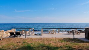 En uteplats vid kusten med sittplatser och bord, med utsikt över havet.