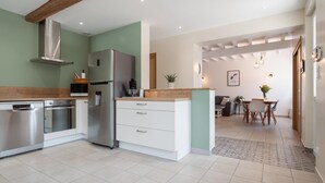 A modern kitchen with stainless steel appliances, a wooden countertop, and a dining area with a table and chairs. - La Maison des Délices (DOSCHES)