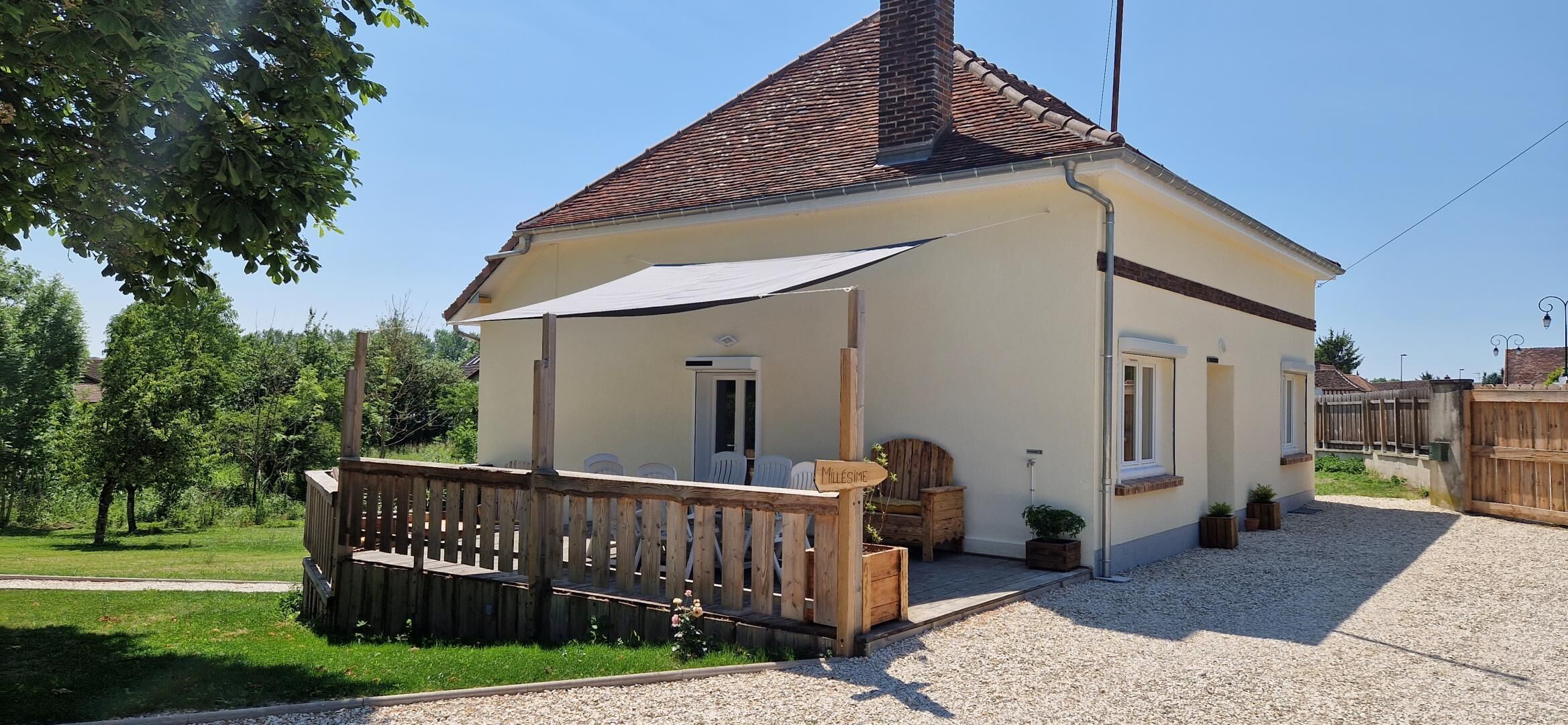 A small, single-story house with a tiled roof, a wooden deck, and a covered patio area.