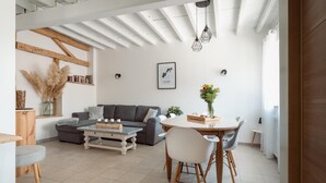 A modern living room with a grey sofa, a wooden coffee table, and a dining area with a round table and chairs. - La Maison des Délices (DOSCHES)