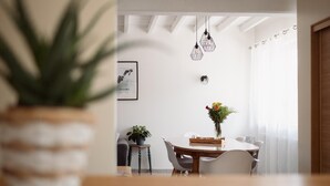 A dining area with a round table, chairs, a potted plant, a wall-mounted light fixture, and a framed picture. - La Maison des Délices (DOSCHES)