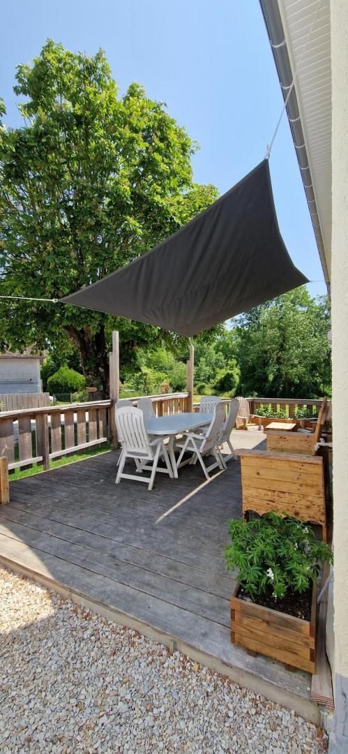 Un patio al aire libre con una mesa y sillas, rodeado de una terraza de madera y un toldo oscuro.