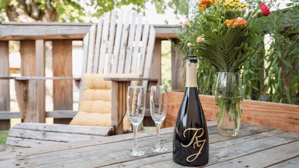 A wooden table with a bottle of champagne, two glasses, and a vase with flowers. - La Maison des Délices (DOSCHES)