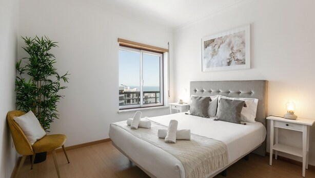 Une chambre à coucher avec un lit, une chaise, une table de chevet, une lampe, une fenêtre et une plante.