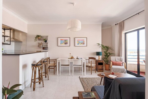 Ein modernes Wohnzimmer mit Essbereich, Küche und großen Fenstern.