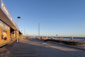 A coastal walkway with a surf camp sign, beach, and ocean view.