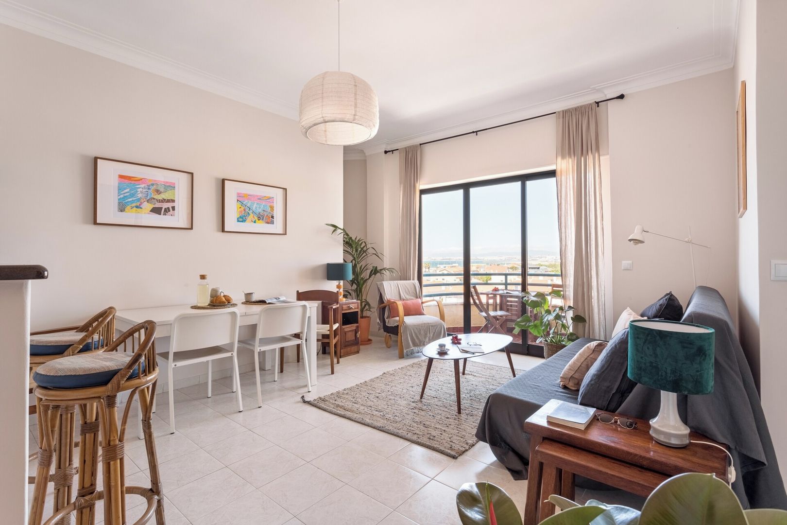 A modern living room with a sofa, dining table, chairs, and a balcony with a view.