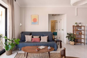 A living room with a sofa, a coffee table, a bookshelf, and a door leading to another room. - Ocean View Apartment in Costa da Caparica (Costa da Caparica)