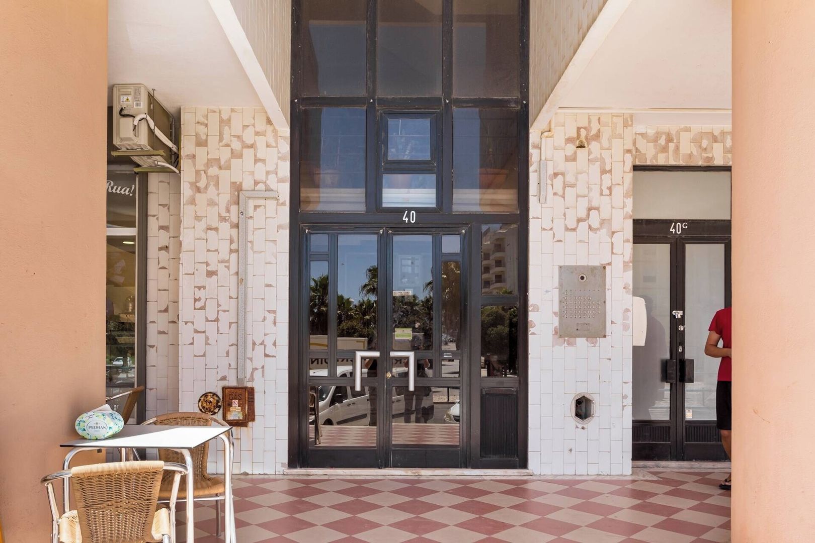 Una entrada de edificio con puerta de vidrio, piso a cuadros y una persona de pie junto a la puerta.