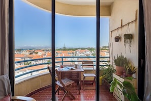 A balcony with a table and chairs, potted plants, and a view of a cityscape.