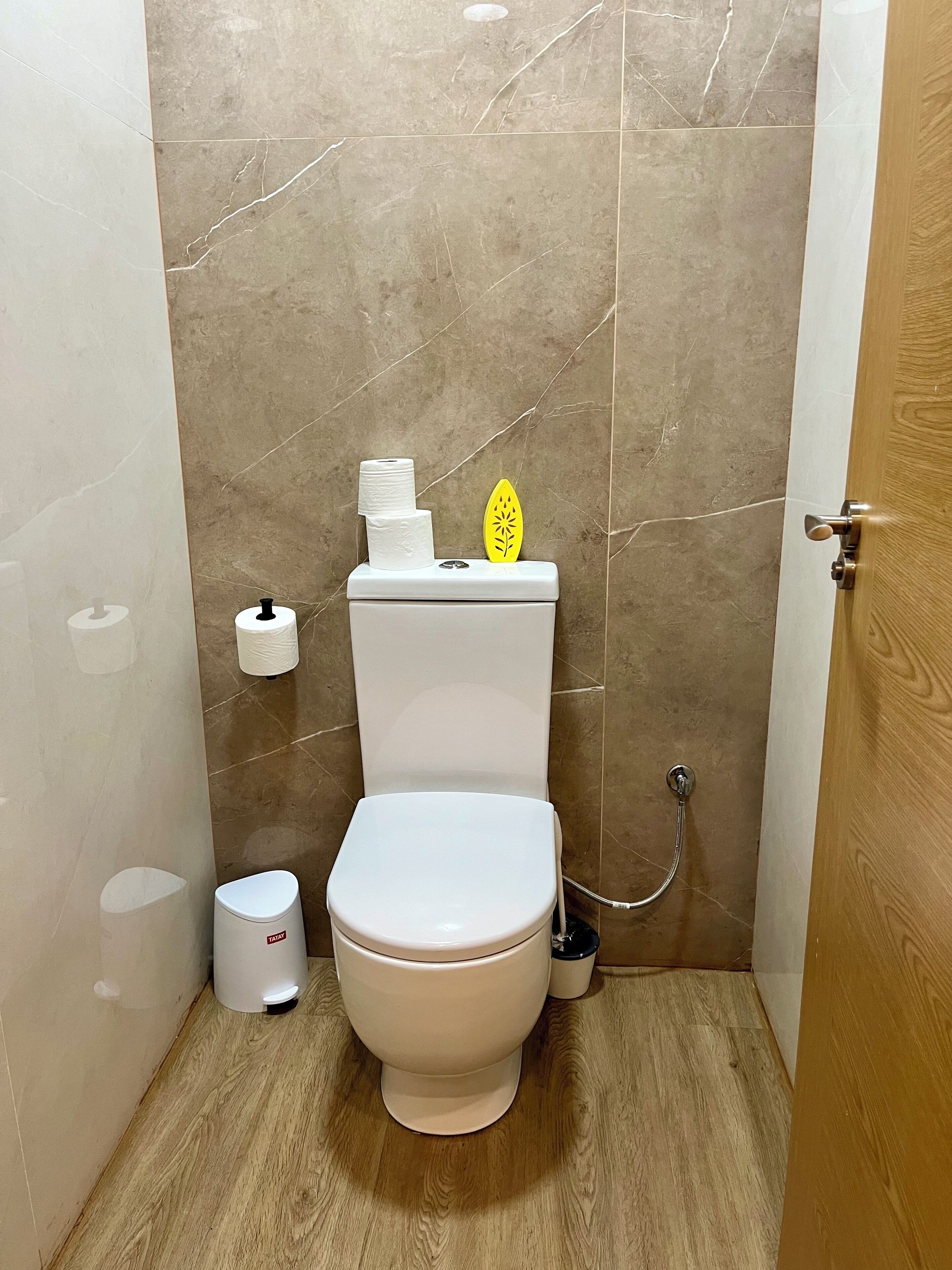 A small bathroom with a toilet, a toilet paper holder, and a trash can.