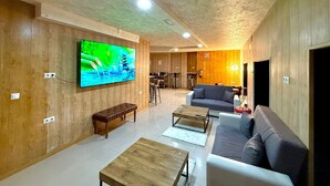 Ein modernes Wohnzimmer mit einem großen Flachbildfernseher, Holzpaneelen, einer Bank, Sofas und einem Couchtisch.