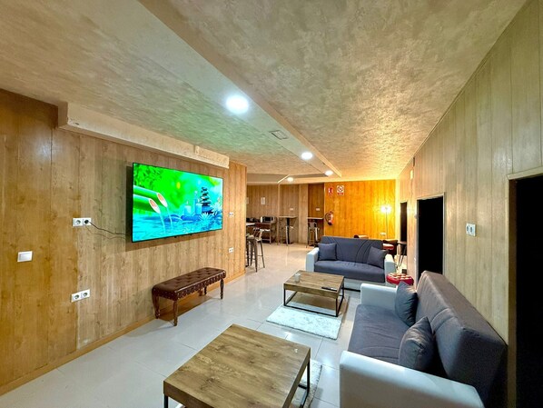 A modern living room with a large flat-screen TV, wooden panel walls, a bench, sofas, and a coffee table. - Velvet Hostel (Madrid)