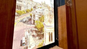 Ein Fenster mit Blick auf eine Stadtlandschaft, eine Bank und eine Tür mit floralem Muster.