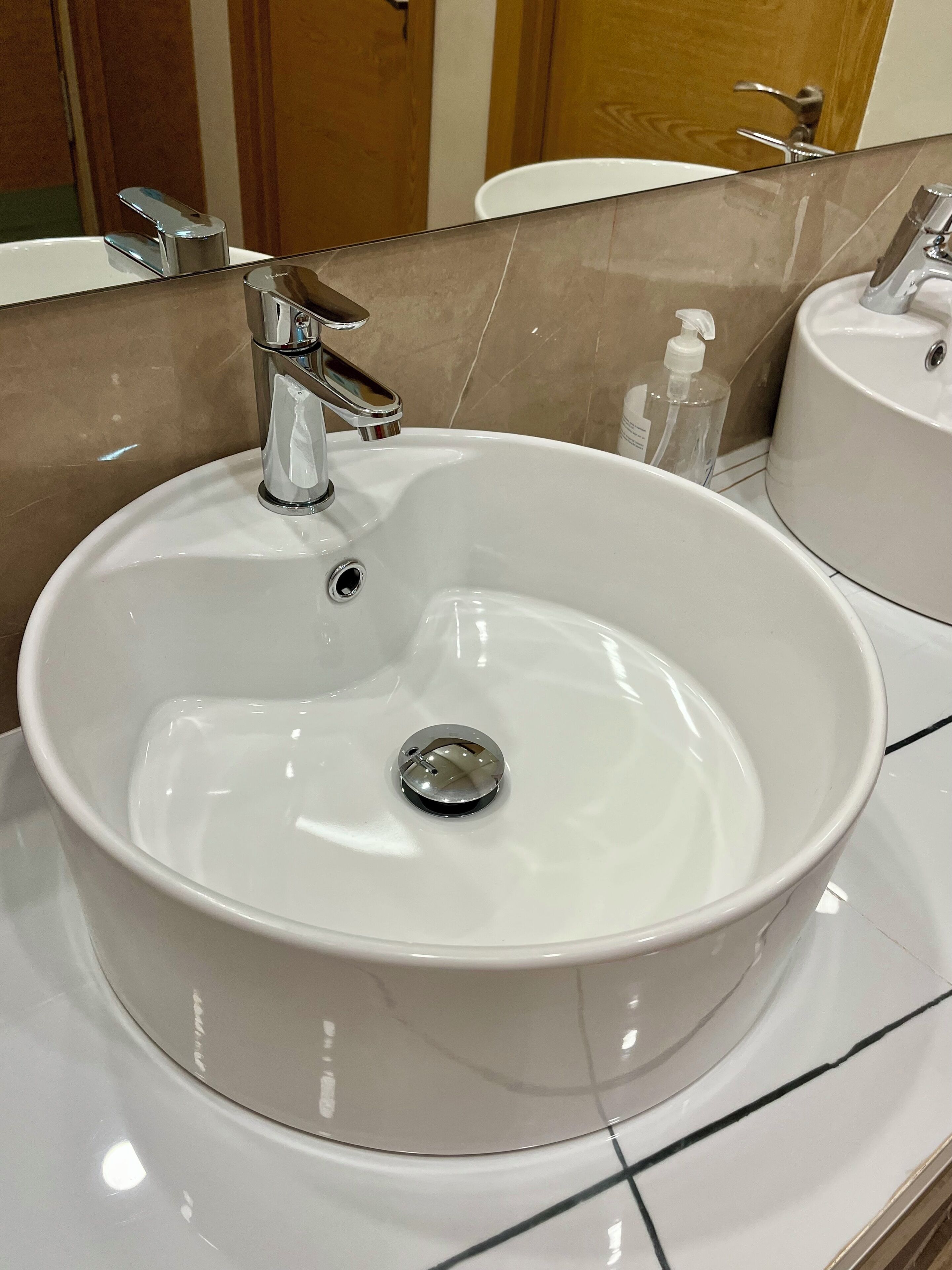 Un lavamanos blanco con grifo cromado, dispensador de jabón y espejo encima.