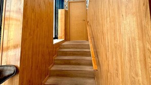 Eine Holztret Treppe führt zu einer Tür, deren Wand mit einem Blumenmuster versehen ist und ein Kronleuchter hängt.