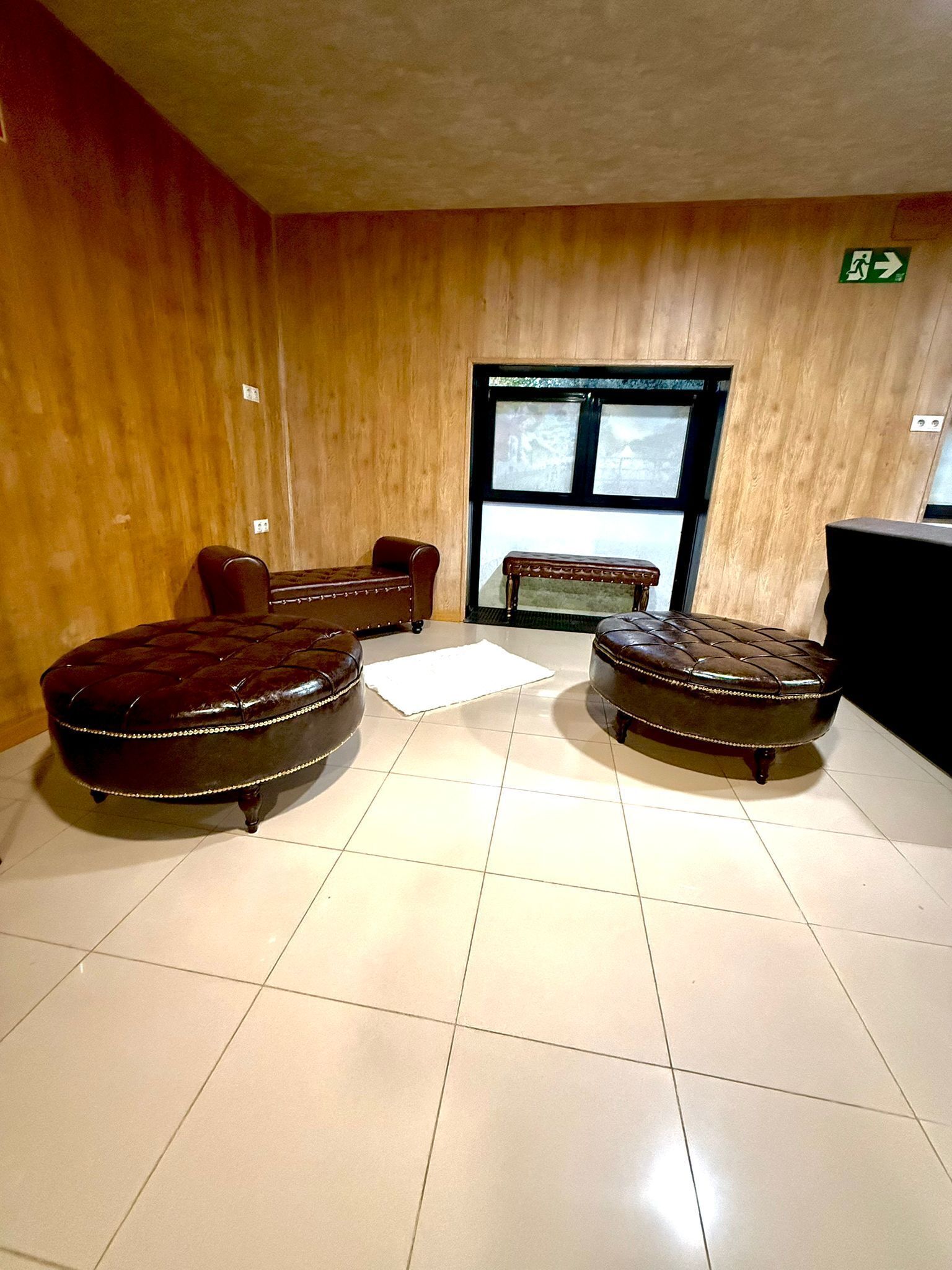 A room with two leather ottomans, a bench, and a window with a view.