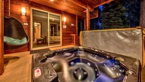 Une cabane en bois dotée d’un bain à remous, d’un fauteuil suspendu et d’une porte-fenêtre coulissante donnant accès à une chambre.