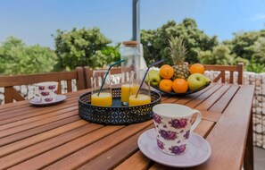 A wooden table with a fruit bowl, a glass of orange juice, a teacup, and a teapot. - Beach front home in Vir with WiFi (Vir)