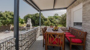 A covered patio with a table and chairs, a barbecue grill, and a stone wall. - Beach front home in Vir with WiFi (Vir)