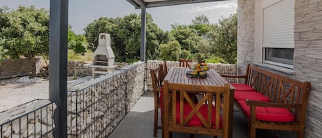 En overdækket terrasse med et bord, stole, grill og en stenvæg.