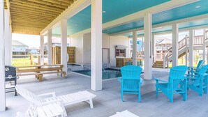 A covered outdoor area with white and blue Adirondack chairs, a wooden bench, and a pool.