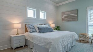 A bedroom with a large bed, two bedside tables, a wall-mounted artwork, and a window with blinds.