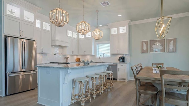 A modern kitchen with white cabinetry, a central island with stools, stainless steel appliances, and pendant lighting.
