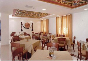 A dining area with multiple tables and chairs, a ceiling with a geometric design, and a wall-mounted decorative item. - Abrahams Herberge (Bethlehem)