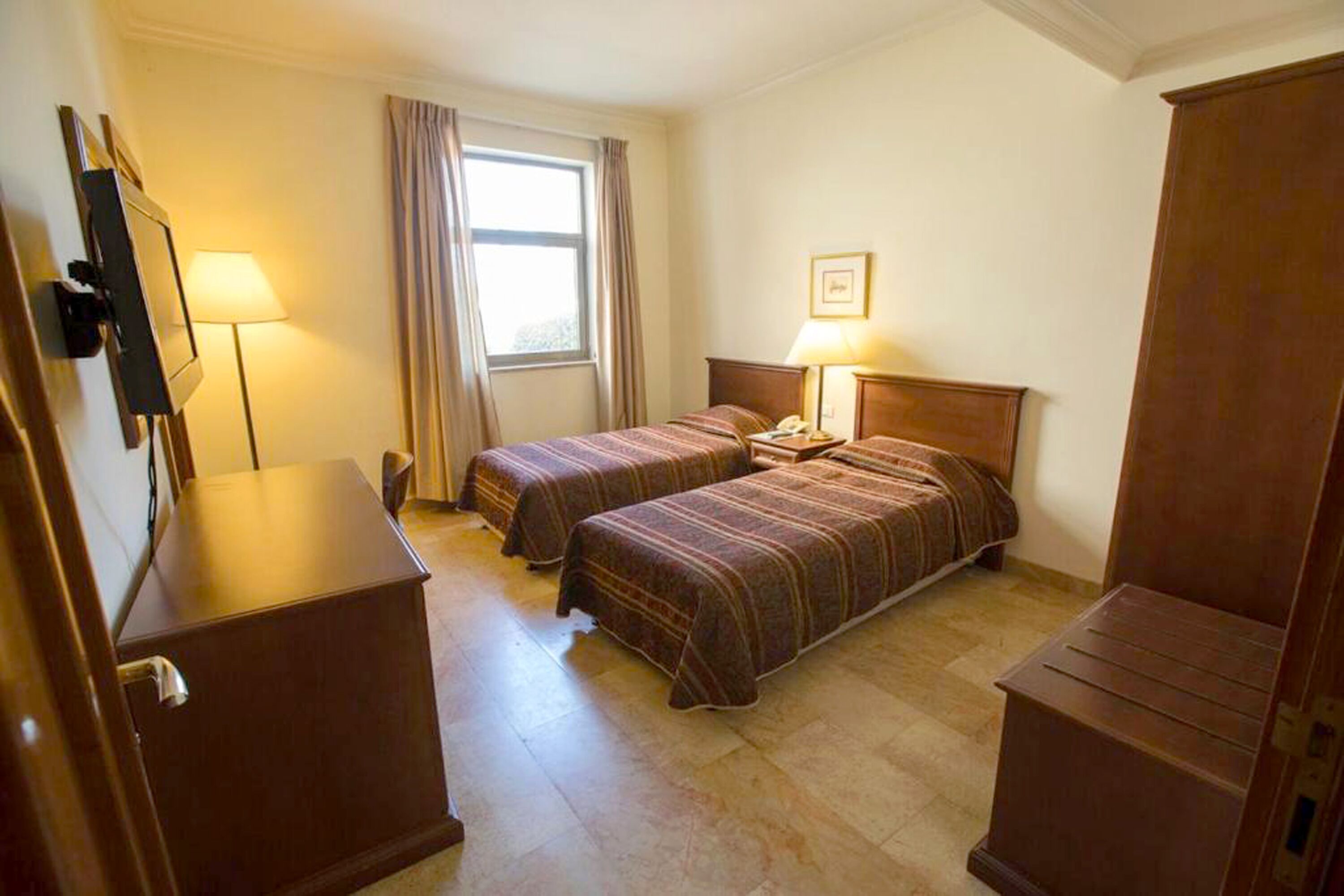 Une chambre d’hôtel avec deux lits, un bureau, une lampe et une armoire.
