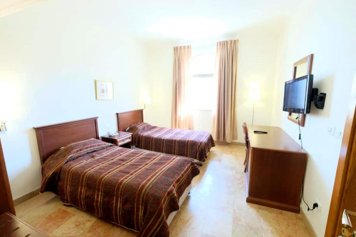 Ett hotellrum med två sängar, ett skrivbord, en tv och ett fönster med gardiner.