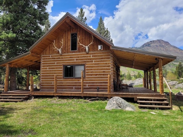 A rustic log cabin with a covered porch, a window, and antlers mounted on the front.