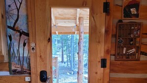 Una puerta de madera con un ventanal, un letrero encima y una pared con un estante y un cuadro.