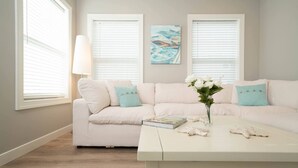 A living room with a white sofa, a coffee table, and a painting on the wall. - Special Moments await you. Stylish. NEW. (South Haven)