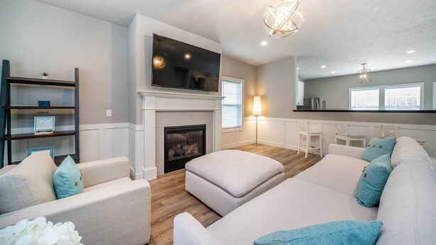 A modern living room with a fireplace, a flat-screen TV mounted above it, and a cozy seating area with a sofa and ottoman. - Special Moments await you. Stylish. NEW. (South Haven)