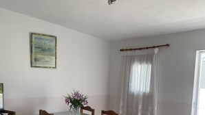 A dining area with a glass table, wooden chairs, a vase with flowers, a framed picture on the wall, and a window with a white curtain. - Pavillon 1ER Etage (Setúbal)