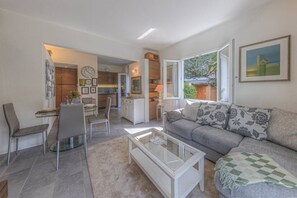 Un salon moderne avec un canapé, une table basse et des fauteuils, une cuisine en arrière-plan et un coin repas avec une table et des chaises.