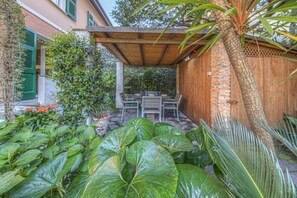 Une terrasse couverte, agréée d’une table et de chaises, entourée d’une végétation luxuriante et d’une clôture en bois.