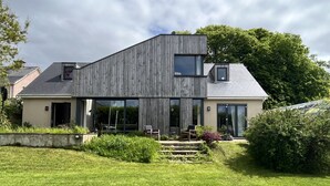 Une maison moderne à deux étages, dotée d’une grande véranda à l’avant, d’une façade en bois et d’une pelouse bien entretenue.