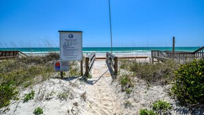 Un panneau indiquant l’accès à la plage, une promenade en bois et une vue sur l’océan.