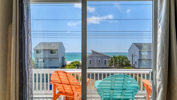 Un balcon avec deux chaises, une vue sur l’océan et des maisons en arrière-plan.