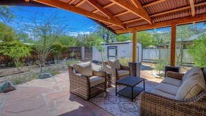 Un patio cubierto con mobiliario de mimbre y piso de piedra, con vistas a un patio trasero con un cobertizo pequeño y árboles.