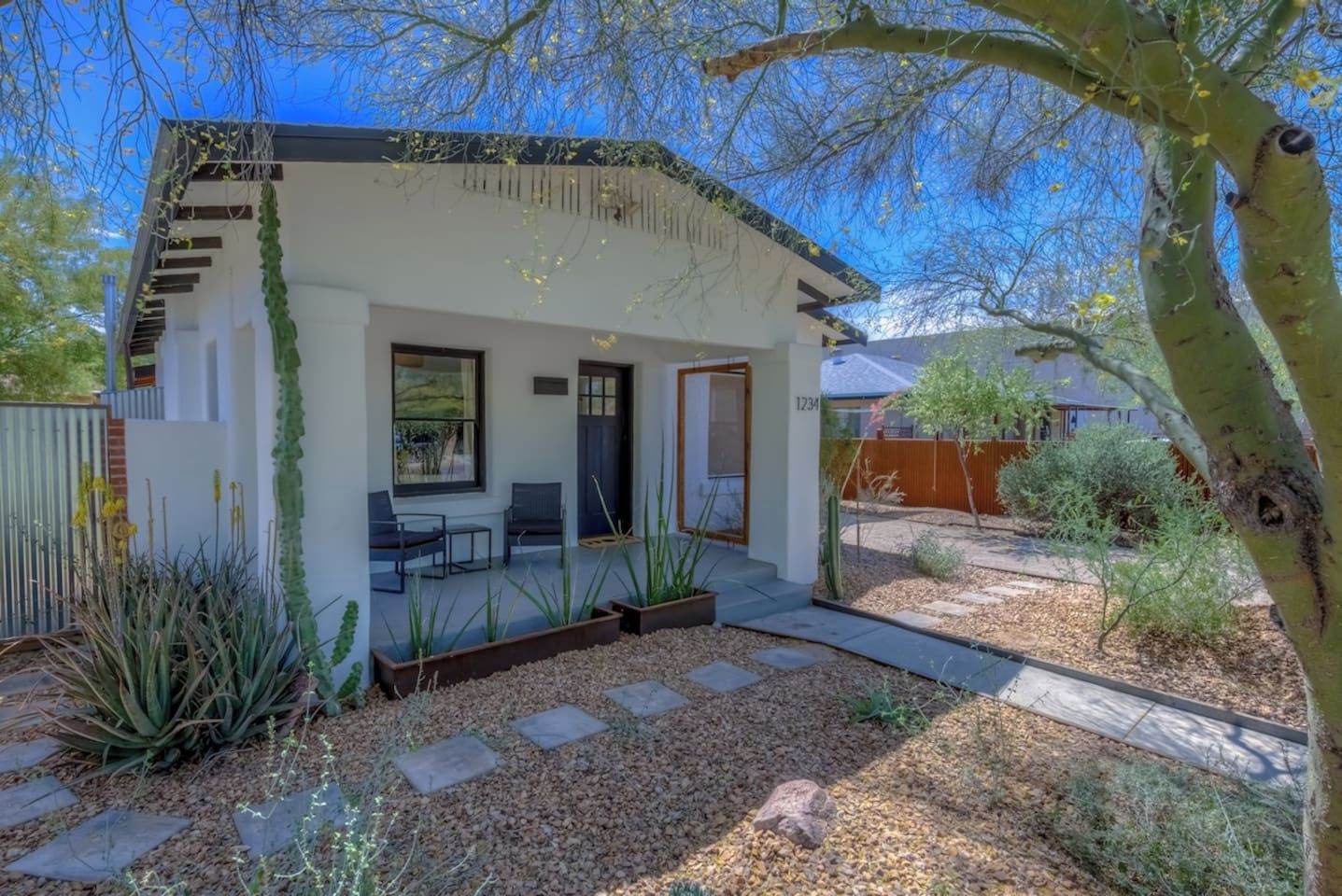 Una casa moderna con un patio, mobiliario de exterior y un jardín.