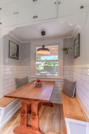 A kitchen with a wooden table, bench seating, white tiled walls, a window, and a hanging pendant light. - Cute bungalow close to UofA (Tucson)