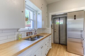 Een keuken met witte kastjes, een roestvrijstalen koelkast en een raam met een plant.