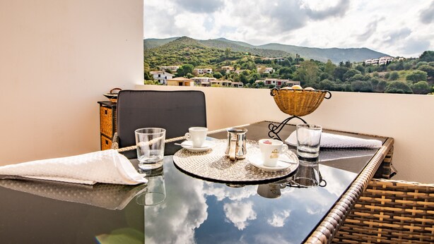 Une table de balcon offrant une vue sur un paysage montagneux, une chaise en osier et un panier en osier.