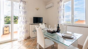 Un coin repas avec une table en verre, des chaises blanches et un téléviseur posé sur un meuble.