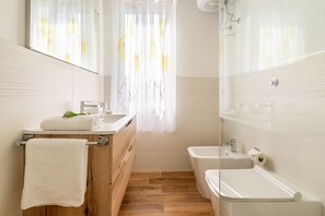 Ein Badezimmer mit einem Holzbadezimmer-Möbel, einem Waschbecken, einem Spiegel, einer Dusche und einer Toilette.